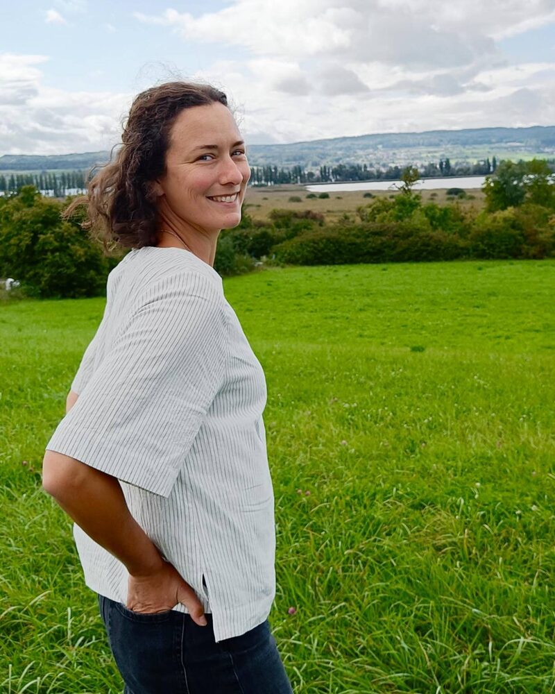 Alexandra Kuritz lächelt in die Kamera, im Hintergrund eine Wiese und ein See